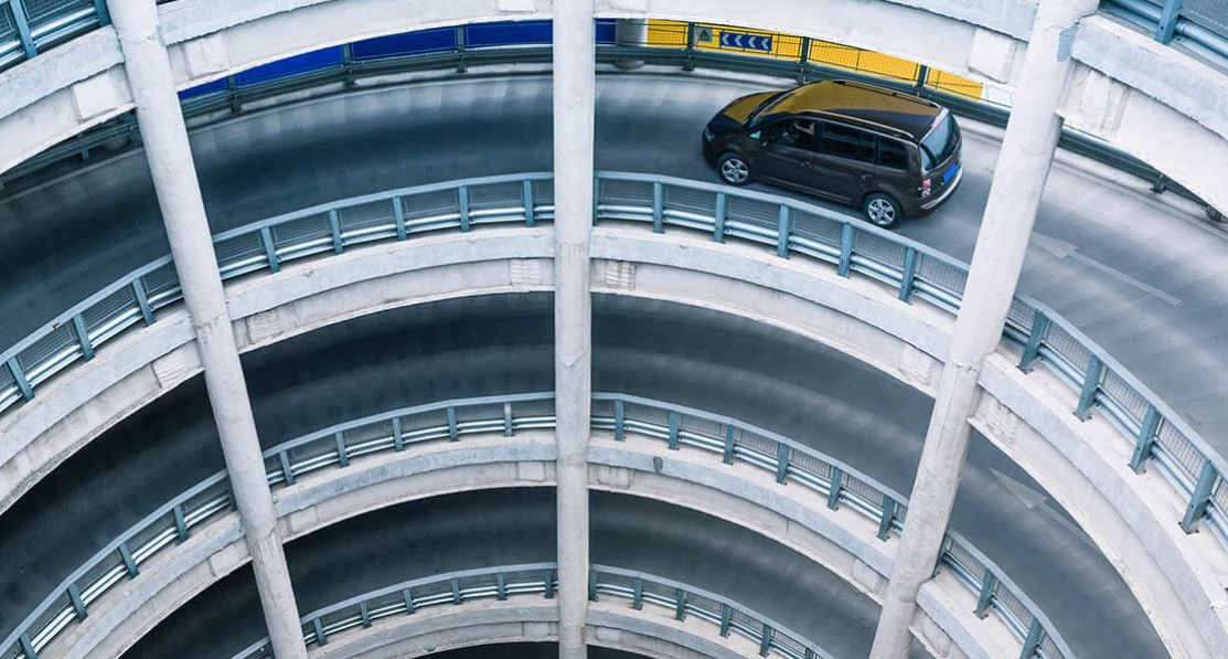 A circular parking ramp that has multiple levels with a car driving on it.